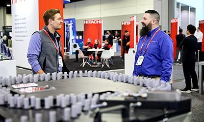 Two men stand beside a large industrial machine, discussing its features and operation